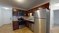 Located at 55 Golfview in Manchester, New Hampshire, this single-floor unit offers a practical and comfortable layout across several well-appointed rooms. The kitchen is a standout feature, outfitted with rich dark-wood cabinetry, granite-style countertops, and a full suite of stainless steel appliances including an electric range, over-the-range microwave, dishwasher, and refrigerator. A tile backsplash and durable tile flooring complete the functional yet attractive design of this space. The living area is generously proportioned, featuring soft wall-to-wall carpeting, neutral cream-toned walls, and a baseboard heating system. A window allows natural light to filter in, offering views of the surrounding greenery. The bedroom continues the same warm, carpeted aesthetic with clean white walls, a closet, and ample space for furnishings. The bathroom is neatly appointed with stone-look tile flooring, a wood-toned vanity with a white countertop, and a full tub and shower combination with a curtain rod. Throughout the unit, the design maintains a consistent, understated palette that creates a clean and welcoming atmosphere. The overall layout is efficient and well-suited for everyday living.