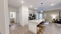 This well-appointed 3-bedroom, 2-bathroom single-story residence offers a thoughtfully designed open-concept layout that maximizes functionality and flow. The combined kitchen, dining, and living area serves as the heart of the home, showcasing light wood-style flooring, recessed lighting, and a large granite-topped kitchen island with bar seating beneath a stylish pendant light. The kitchen is equipped with stainless steel appliances, grey shaker-style cabinetry, and a dedicated pantry for additional storage. The living area features a ceiling fan and a warm, inviting atmosphere filled with natural light. Each of the three bedrooms offers comfortable proportions, with the primary bedroom featuring a large window with blinds and ample natural light. Three closets, including walk-in style storage with wire shelving systems, provide generous organization space. Both bathrooms are finished with granite-topped vanities, grey cabinetry, and full tub-shower combinations with white tile surrounds. One bathroom includes a backlit vanity mirror for an added modern touch. A dedicated laundry area and in-unit pantry add to everyday convenience. The private balcony overlooks a community pool, offering a relaxing outdoor retreat.