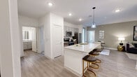 This well-appointed 3-bedroom, 2-bathroom single-story residence offers a thoughtfully designed open-concept layout that maximizes functionality and flow. The combined kitchen, dining, and living area serves as the heart of the home, showcasing light wood-style flooring, recessed lighting, and a large granite-topped kitchen island with bar seating beneath a stylish pendant light. The kitchen is equipped with stainless steel appliances, grey shaker-style cabinetry, and a dedicated pantry for additional storage. The living area features a ceiling fan and a warm, inviting atmosphere filled with natural light. Each of the three bedrooms offers comfortable proportions, with the primary bedroom featuring a large window with blinds and ample natural light. Three closets, including walk-in style storage with wire shelving systems, provide generous organization space. Both bathrooms are finished with granite-topped vanities, grey cabinetry, and full tub-shower combinations with white tile surrounds. One bathroom includes a backlit vanity mirror for an added modern touch. A dedicated laundry area and in-unit pantry add to everyday convenience. The private balcony overlooks a community pool, offering a relaxing outdoor retreat.