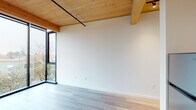 Located at 7373 N Philadelphia Avenue in Portland, Oregon, this thoughtfully designed single-floor space blends modern aesthetics with warm natural materials. The interior is immediately distinguished by its striking exposed wood beam ceiling with tongue-and-groove planking, which adds warmth and architectural character throughout the open living area. Light-toned hardwood-style flooring complements the natural wood overhead, creating a cohesive and inviting palette.

Floor-to-ceiling black-framed windows form a dramatic corner feature in the main living area, flooding the space with natural light and offering elevated views of the surrounding Portland neighborhood and tree canopy. A ceiling-mounted track lighting system provides flexible illumination, while a wall-mounted mini-split unit ensures year-round climate comfort.

The kitchen is efficiently designed with two-toned cabinetry — muted teal lower cabinets paired with white uppers — complemented by a clean white countertop and a full suite of stainless steel appliances, including a refrigerator, electric range, dishwasher, and range hood. In-unit laundry is also present, adding everyday convenience.

The bathroom is clean and functional, featuring a tub-shower combination, a dark-cabinetry vanity with a white sink, and a large mirror. The overall ambiance of the space is bright, modern, and well-appointed, with a strong emphasis on natural materials and urban views.