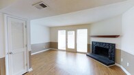 This two-story home offers a comfortable and functional layout designed for everyday living. The main living area is a standout space, featuring warm hardwood-style flooring that extends throughout, creating a cohesive and inviting atmosphere. A classic fireplace with a dark stone surround and a rich wood mantel serves as the focal point of the room, adding both character and warmth. Large sliding glass doors and adjacent sidelights flood the space with abundant natural light while providing direct access to the outdoors, making the living area feel open and airy. The walls feature a two-tone paint scheme with a neutral upper tone and a warm taupe lower half, accented by clean white trim and baseboards that lend a crisp, polished look. A textured ceiling adds a subtle traditional detail overhead. The overall ambiance of the main level is bright, clean, and move-in ready, offering a blank canvas for personalization. The second floor expands the living space further, accommodating additional rooms suited for bedrooms, offices, or flexible use. Together, the two floors provide a well-rounded and spacious environment suitable for a variety of lifestyles.