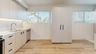 Located at 2601 S Hoover St in Los Angeles, CA, this efficiently designed studio unit makes excellent use of its compact footprint. The space features light hardwood-style flooring throughout, crisp white walls, and recessed lighting that contribute to a clean, modern aesthetic.

The sleeping area is anchored by a built-in platform bed with integrated under-bed storage drawers, maximizing functionality without sacrificing space. A wall-mounted flat-screen TV and a dedicated desk with an ergonomic chair provide both comfort and a practical workspace. A wall-mounted mini-split air conditioning unit ensures year-round climate control.

The kitchen is well-appointed with gray flat-front cabinetry, subway tile backsplash, and a full suite of stainless steel appliances including a full-size refrigerator, gas range, built-in microwave, and dishwasher. A double-basin sink with a modern faucet completes the thoughtfully designed cooking area. A tall freestanding wardrobe cabinet provides additional storage near the windows, which allow natural light and views of surrounding greenery to filter into the space. The unit also includes an electrical panel conveniently accessible from the main living area.
