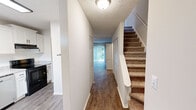 This two-story, two-bedroom, two-bathroom home in Knoxville, Tennessee is thoughtfully laid out across two floors. The main level features a welcoming hallway with rich hardwood-style flooring that flows throughout, a bright and updated kitchen, and a utility room. The kitchen is a standout feature, boasting white shaker-style cabinetry with matte black hardware, granite-look countertops, a subway tile backsplash, a deep black undermount sink, and stainless steel appliances including a dishwasher and refrigerator. Natural light filters in through a window, adding to the kitchen's clean, modern aesthetic. A spacious living area on the main floor offers ample room and double closet storage, completing the lower level. Carpeted stairs lead to the upper floor, where both bedrooms are located. The generously sized primary bedroom features a large window with outdoor views and a double-door closet with built-in shelving. The second bedroom is comfortably sized with its own window and soft carpeting throughout. Both bathrooms are well-appointed, with the upper bath featuring a granite vanity top, white cabinetry, and elegant matte black fixtures. Textured ceilings are found throughout the home, contributing to its classic character.
