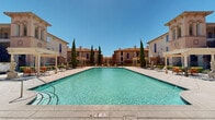 Located at 2000 Villa Dr in Pittsburg, California, this Mediterranean-inspired community showcases a striking architectural design characterized by warm terracotta-toned stucco exteriors, arched windows, decorative tower elements, and clay tile rooflines. The buildings are arranged around a central outdoor amenity area that serves as the heart of the community.

At the center of the outdoor space is a generously sized resort-style swimming pool with pristine turquoise water, surrounded by a spacious pool deck furnished with lounge chairs and seating areas ideal for relaxation. Pergola-covered shade structures are positioned poolside, offering comfort during sunny California days. Tall, slender Italian cypress trees are strategically placed throughout the grounds, reinforcing the Mediterranean aesthetic and adding vertical interest to the landscape.

The community's grounds are meticulously maintained, featuring manicured hedgerows, vibrant flowering plants, and well-kept walkways lined with ornamental fencing and decorative statuary. A prominent clubhouse building anchors the pool area with a grand arched entrance and large windows that allow abundant natural light. Rolling hills provide a scenic backdrop visible from the property, enhancing the overall sense of openness. The cohesive design and thoughtfully curated outdoor spaces create a resort-like ambiance throughout the community.
