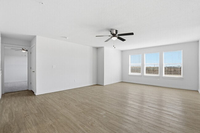 Bright and spacious living room with sleek wood flooring, large windows offering natural light, and a modern ceiling fan. - Oaks at Mustang