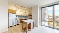Located at 180 High Park Lane in Silver Spring, Maryland, this 2-bedroom, 1-bathroom residence offers a thoughtfully designed single-floor layout with modern finishes throughout. The kitchen serves as a standout feature, showcasing two-tone cabinetry with white upper cabinets and warm wood-grain lower cabinets, a striking mosaic tile backsplash in cool blue and gray tones, white quartz countertops, and a full suite of stainless steel appliances including a refrigerator, gas range, microwave, and dishwasher. Track lighting illuminates the space, and a freestanding kitchen island with a matching wood-grain finish provides additional prep and storage space. Large floor-to-ceiling windows allow natural light to fill the area and offer views of the surrounding exterior. Light wood-style flooring runs through the main living areas, lending warmth and continuity. The two bedrooms feature neutral carpet and clean white walls, creating a calm and versatile environment. The bathroom is finished with large-format tile flooring, a tiled tub-and-shower combination with a mosaic accent stripe, a dark-stained vanity with a white countertop, and a large mirror. Two hallways and a dedicated closet complete the efficient layout of this Silver Spring residence.