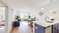 This well-designed 2-bedroom, 1-bathroom unit offers a thoughtful open-concept layout that maximizes every square foot of living space. Warm hardwood-style flooring flows continuously throughout, unifying the kitchen, dining, and living areas into one cohesive space. The kitchen is a standout feature, showcasing bold navy cabinetry paired with crisp white upper cabinets, quartz countertops, a peninsula with bar seating, and a full suite of stainless steel appliances including a refrigerator, range, microwave, and dishwasher. Pendant lighting adds a modern touch overhead. The open living area is bathed in natural light from large windows, creating a bright and airy atmosphere. The primary bedroom offers a comfortable footprint with a sliding-door closet and convenient access to the shared hallway and bathroom. The second bedroom mirrors the clean, light-filled aesthetic found throughout the unit. The bathroom features classic white subway tile surrounding a full soaking tub and shower, complemented by a white vanity and hardwood-style flooring. A hallway connects the private and shared spaces efficiently. The unit's clean white walls, modern finishes, and consistent flooring create a cohesive, contemporary ambiance throughout.