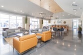 Located at 5500 Freedom Lane in Greensboro, NC, this single-story community clubhouse offers a thoughtfully designed, multi-functional space tailored to both recreation and productivity. The welcoming lobby greets visitors with polished concrete floors, soaring ceilings, and a striking sculptural centerpiece, setting the tone for the refined aesthetic found throughout.

The expansive lounge and social area features vaulted ceilings with a wood-paneled tray accent, large ceiling fans, and a dramatic stone-clad fireplace with a mounted flat-screen TV — creating a warm yet contemporary gathering space. Floor-to-ceiling glass doors open toward an outdoor pool area, flooding the interior with natural light.

The clubhouse kitchen is well-appointed with warm wood cabinetry, granite countertops, a textured tile backsplash, stainless steel appliances, and polished concrete flooring, complemented by stylish pendant lighting.

The fitness center is generously sized, offering a wide array of cardio equipment including treadmills, ellipticals, and spin bikes, along with a mirrored studio area equipped with a flat-screen TV, ceiling fan, and light wood flooring — ideal for group workouts or individual training.

Business amenities include a bright co-working area with dedicated workstations and a formal conference room featuring a large wood table, mixed seating, display screen, and ample natural light.