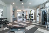 Located at 2245 Interstate North Pkwy SE in Atlanta, GA, this single-floor fitness center offers a comprehensive and well-appointed workout facility designed to accommodate a wide range of exercise routines. The space is organized into several distinct zones, each serving a specific fitness purpose.

The main gym area features an extensive selection of strength-training machines, including cable machines, weight benches, and selectorized equipment, all set on a geometric patterned carpet with generous natural light streaming in through large windows. Full-length mirrors line the walls, enhancing the sense of openness throughout.

A dedicated cardio room houses a row of treadmills, elliptical machines, upright bikes, and a stair climber, positioned facing windows that allow views of the surrounding greenery. Ceiling fans and recessed lighting keep the environment comfortable during workouts.

A separate multi-use area includes a punching bag, boxing equipment, a cable tower, and free weights, providing space for high-intensity and functional training. An additional room is finished as a sports simulation suite, featuring a large projection screen, turf flooring, and various sport props for immersive training experiences.

A welcoming entryway corridor with warm accent lighting, wood-style flooring, and louvered storage doors connects the various zones, giving the facility a polished, modern aesthetic throughout.