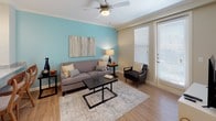 This single-floor residence offers a thoughtfully designed layout that balances comfort and functionality across its key living areas. The bedroom is a warm and inviting retreat, featuring soft gold-toned walls, plush carpeting, and abundant natural light streaming through large windows dressed with sheer curtains and blinds. A ceiling fan adds a practical touch, while the well-proportioned space easily accommodates generous furnishings. The kitchen is a standout feature, showcasing rich dark cabinetry, granite countertops, and a full suite of stainless steel appliances including a refrigerator, range, and microwave. Light wood-style flooring flows throughout, complementing the kitchen's peninsula with a built-in sink — ideal for casual dining or meal prep. The living area is bright and welcoming, anchored by a distinctive teal accent wall, crown molding, and a ceiling fan overhead. Natural light pours in through large windows and a glass door, creating an airy atmosphere. The bathroom continues the home's refined aesthetic with dark cabinetry, granite countertops, a wide vanity mirror with Hollywood-style lighting, tile flooring, and a walk-in shower. Together, these spaces create a cohesive and comfortable living environment with consistent, attractive finishes throughout.