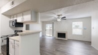 This single-floor, 2-bedroom, 2-bathroom home features a well-designed open-concept layout that seamlessly connects the living room and kitchen. The living room is a standout space, highlighted by a tile-surround fireplace, wood-look plank flooring, a ceiling fan with light fixture, and a textured ceiling. A sliding glass door opens to a private balcony, flooding the room with natural light. An additional window with blinds further brightens the space.

The kitchen runs in a galley-style configuration and is equipped with gray cabinetry, a mosaic tile backsplash, light stone countertops, stainless steel appliances including a refrigerator, microwave, and range, as well as a double-basin sink. A pass-through counter connects the kitchen to the living area.

Both bedrooms feature plush carpeting, neutral walls, a textured ceiling, and generous closet space. The primary bedroom includes a walk-in closet with built-in shelving and hanging rods. The second bedroom offers a bright window with natural light. The bathrooms are finished with white tile surrounds accented by a decorative mosaic border. A dedicated utility room and three total closets provide practical storage throughout the home.