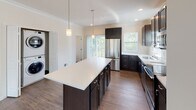 Located at 300 Old Mill Rd in Oakdale, PA, this three-floor residence offers a clean, modern aesthetic with thoughtful finishes throughout. The open-concept main living area features wood-look flooring, crown molding, and multiple windows that flood the space with natural light while offering pleasant outdoor views. A ceiling fan adds comfort to the generous living room.

The kitchen is a standout feature, boasting dark cabinetry, a large center island with a crisp white countertop, pendant lighting, and a full suite of stainless steel appliances including a refrigerator, electric range, microwave, and dishwasher. Wood-look flooring continues seamlessly through this space, and a sliding glass door provides access to an outdoor balcony.

Carpeted bedrooms offer a soft, comfortable feel with neutral walls and ample space. The bathrooms are well-finished with dark vanity cabinetry, white countertops, and wood-look flooring. One bathroom features a walk-in glass-door shower, another includes a soaking tub with classic black-and-white mosaic tile flooring and a window with outdoor views, while a third provides a vanity with a mirror.

An in-unit stacked washer and dryer is conveniently located near the kitchen. The multi-floor layout, visible in the dollhouse view, showcases a staircase connecting the levels and a versatile, functional floor plan throughout.