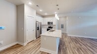 Located in Charlotte, NC, this well-appointed one-bedroom, one-bathroom unit offers a thoughtfully designed single-floor layout with modern finishes throughout. The open-concept kitchen serves as the centerpiece of the living space, showcasing white shaker cabinetry, a classic subway tile backsplash, stainless steel appliances including a French door refrigerator, and a large granite-topped island with an undermount sink and pendant lighting overhead. Wood-style plank flooring flows through the main living areas, complementing the bright, neutral color palette. The living area receives natural light through large windows and French doors, and is equipped with a ceiling fan for year-round comfort. The bedroom features plush carpeting, a ceiling fan, and a window with natural light. It is accompanied by a spacious walk-in closet outfitted with wire shelving for organized storage. The bathroom offers a granite-topped vanity with white cabinetry, a framed mirror, and a walk-in shower with a glass door and wood-look tile flooring. A dedicated laundry room houses a full-size Whirlpool washer and dryer set with overhead wire shelving, adding everyday convenience to this well-rounded unit.