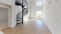 This contemporary two-story residence blends modern design with functional living across two well-appointed floors. The main level is anchored by a dramatic open living area boasting soaring double-height ceilings and large picture windows that flood the space with natural light and offer elevated outdoor views. Light-toned hardwood flooring runs throughout the main level, complementing the bright, neutral palette of the walls. A sleek, modern kitchen features dark wood cabinetry with a textured grain finish, white quartz countertops, a tile backsplash, and a full suite of stainless steel appliances including a gas range, microwave, and refrigerator. A bold black spiral staircase serves as a striking architectural centerpiece, connecting the main level to the upper floor. Upstairs, carpeted bedrooms provide a comfortable retreat, each equipped with ceiling fans and generous windows that invite natural light and outdoor views. The primary bedroom includes a walk-in closet and direct access to an en-suite bath. The bathrooms feature warm wood-look vinyl flooring, dark vanity cabinetry with quartz countertops, and full tub-shower combinations accented by floor-to-ceiling gray tile surrounds. A spacious upper landing with clerestory windows adds an airy, open feel to the second floor.