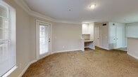 Located at 100 River Ridge Dr in Canton, GA, this one-bedroom, one-bathroom residence offers a thoughtfully designed single-floor layout that maximizes functionality and comfort. The open-concept kitchen and living area forms the heart of the home, where warm wood-toned cabinetry, light countertops, and a peninsula with a double sink create a practical and inviting space. White appliances including a refrigerator, range, and dishwasher are seamlessly integrated into the kitchen. Crown molding accents the living area, which features plush carpeting and a door leading to a private balcony, allowing natural light to pour in. A built-in desk nook adds a convenient workspace within the living area. The carpeted bedroom is generously sized, benefiting from a large window with outdoor views and access to a well-organized walk-in closet with wire shelving. The bathroom features a soaking tub with tiled surround and brushed nickel grab bars. A dedicated laundry room with tile flooring, wire shelving, and washer/dryer hookups adds everyday convenience. Three closets throughout the unit provide ample storage, completing this well-appointed residence.