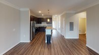 This two-story space is designed with a clean, functional aesthetic throughout. The main living area is anchored by a wood-look flooring that extends from the open-concept kitchen into the living room. Crown molding and a ceiling fan add refined detail to the living room, which also features a stone-accented fireplace flanked by windows that allow natural light to filter in.

The kitchen is well-equipped with dark espresso cabinetry, granite countertops, and a full suite of stainless steel appliances, including a refrigerator, range, and microwave. A central island with pendant lighting above provides additional prep space and casual seating.

Multiple bedrooms are finished with neutral-toned carpet and ceiling light fixtures, offering a comfortable and quiet atmosphere. One bedroom benefits from corner windows that bring in ample natural light.

The bathrooms are distinctly appointed: one features a glass-enclosed walk-in shower with white subway tile and a single vanity, while another includes a full soaking tub with a shower, dark tile flooring, and dark cabinetry. A half bath with hardwood-style flooring and brushed nickel fixtures completes the layout.