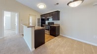 Located at 650 W Flintlake Ct in Myrtle Beach, SC, this single-floor home offers a well-designed, open-concept layout that seamlessly connects the kitchen and living areas. The kitchen is equipped with dark espresso cabinetry, granite-style countertops, stainless steel appliances including a refrigerator and range, and a peninsula breakfast bar that provides both additional counter space and a natural division between the kitchen and the adjoining living area. The living room is generously sized, featuring vaulted ceilings that enhance the sense of openness, a ceiling fan, and a sliding glass door that invites natural light and provides outdoor access. Plush wall-to-wall carpeting runs throughout the living spaces, while the kitchen and bathroom areas feature warm hardwood-style flooring. The bedrooms are comfortably proportioned, with large windows fitted with blinds that allow for ample natural light and privacy. The bathroom is well-appointed with a dark wood vanity, solid-surface countertop, a full tub and shower combination, and hardwood-style flooring. The home's neutral color palette and clean architectural lines create a bright, welcoming atmosphere throughout.