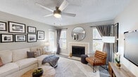 The Birch is a thoughtfully designed one-bedroom, one-bathroom residence in Memphis, TN, offering a comfortable and cohesive single-floor layout. The living room serves as the centerpiece of the home, featuring a tiled wood-burning fireplace flanked by multiple windows that fill the space with natural light. A ceiling fan overhead, textured ceiling, and neutral gray walls create a warm, inviting atmosphere complemented by hard-surface flooring. The bedroom is generously sized, outfitted with plush carpeting, a ceiling fan, and direct access to a dedicated walk-in closet, providing ample storage. Sliding doors in the bedroom offer additional natural light and outdoor access. The bathroom features wood-look vinyl flooring, a tub-shower combination, and a vanity with a granite-style countertop, offering a clean and functional design. A kitchen and dining area are also present, as seen in the dollhouse view, completing the practical layout. Throughout the home, a consistent neutral palette, modern fixtures, and thoughtful details contribute to a polished, move-in-ready aesthetic suited for comfortable everyday living.
