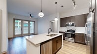 This single-story, 2-bedroom, 3-bathroom unit is thoughtfully designed with a modern aesthetic and an efficient, open layout. The kitchen serves as a central focal point, featuring a large island with a double-basin sink, white quartz countertops, and dark espresso cabinetry. A white subway tile backsplash complements the stainless steel appliances, which include a refrigerator, range, microwave, and dishwasher. Pendant lighting and a track light fixture illuminate the space, which flows seamlessly into the living area. The living room is bright and open, with wood-style flooring, a ceiling fan, and French doors that bring in natural light and provide outdoor access. Both bedrooms continue the wood-style flooring and offer clean, neutral walls with ample natural light from large windows fitted with horizontal blinds. Each room includes closet storage. The three bathrooms are finished with dark hardware fixtures, wood-toned vanities with quartz countertops, and tub-shower combinations wrapped in large-format marble-look tile. A hallway connects the main living areas to the bedrooms, giving the unit a well-organized, functional flow throughout.