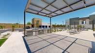 Located at 15400 W Roosevelt St in Goodyear, Arizona, this contemporary residential community showcases a thoughtfully designed exterior environment built for the Sonoran Desert climate. The multi-story buildings feature a modern Southwest architectural style, blending stucco facades with stone accents, private balconies, and large windows that invite natural light throughout.

The grounds are extensively landscaped with drought-tolerant desert plantings, decorative gravel, and strategically placed trees that provide shade and visual interest without demanding excessive water. A dedicated outdoor social area serves as a central gathering hub, complete with a concrete fire pit surrounded by Adirondack-style chairs and overhead string lighting that creates a warm ambiance for evening gatherings.

A shaded pergola area offers additional outdoor seating alongside built-in grilling stations, ideal for outdoor dining and entertaining. Raised wooden garden beds under a shade sail provide residents the opportunity to grow their own plants. A lush turf lawn offers a green, open recreational space. Ample parking is available throughout the property, including covered carport structures and accessible parking spaces, all connected by well-maintained walkways and sidewalks designed for convenient, safe pedestrian circulation across the community.
