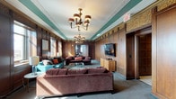 Located in a distinguished building in downtown St. Louis, this Executive Lounge blends historic architectural character with modern functionality across a single floor. Rich, dark wood paneling lines the walls throughout much of the space, accented by ornate carved friezes and teal-painted crown moldings that speak to the building's storied heritage.

The lounge areas are thoughtfully appointed with plush seating arrangements, including velvet sofas and accent chairs in jewel tones, anchored by glass coffee tables and illuminated by elegant brass chandeliers. Large windows admit generous natural light and frame views of the St. Louis skyline. A more intimate sitting room offers additional lounge seating alongside a flat-screen television and warm ambient lighting.

The space includes two well-equipped kitchens featuring dark cabinetry, white countertops, stainless steel appliances, and a breakfast bar with seating. Meeting needs are addressed by a formal boardroom with a large white conference table and ergonomic seating, as well as a smaller meeting room with a glass-top table and contemporary red chairs. Wide-paneled entry corridors with coffered ceilings and tiled flooring create a grand sense of arrival throughout.