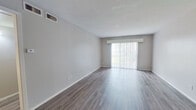 This single-floor unit offers a well-organized layout comprising one bedroom, two bathrooms, a living room, kitchen, and hallway. The living room is a notable highlight, featuring wood-style laminate flooring in a warm gray-brown tone, neutral gray walls, and a large sliding glass door fitted with vertical blinds that allows abundant natural light to fill the space. A ceiling fan is present, adding to the room's functionality.

The kitchen follows a classic galley configuration, outfitted with white cabinetry providing ample storage, light countertops, a double-basin sink, and white appliances including a range and full-size refrigerator. Light-toned wood-style flooring complements the clean, bright aesthetic.

The bedroom is a comfortable size, featuring the same wood-style flooring found throughout, a window with blinds offering natural light, and a full-width sliding closet with clean white doors for generous storage.

Both bathrooms are functionally appointed. One includes a full soaking tub with shower surround, toilet, and a vanity with dark granite-style countertop and wood-toned cabinetry. Neutral tones and straightforward finishes carry throughout.

Overall, the unit presents a clean, move-in-ready aesthetic with consistent flooring and a cohesive neutral color palette throughout.