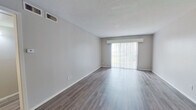 This single-floor unit offers a well-organized layout comprising one bedroom, two bathrooms, a living room, kitchen, and hallway. The living room is a notable highlight, featuring wood-style laminate flooring in a warm gray-brown tone, neutral gray walls, and a large sliding glass door fitted with vertical blinds that allows abundant natural light to fill the space. A ceiling fan is present, adding to the room's functionality.

The kitchen follows a classic galley configuration, outfitted with white cabinetry providing ample storage, light countertops, a double-basin sink, and white appliances including a range and full-size refrigerator. Light-toned wood-style flooring complements the clean, bright aesthetic.

The bedroom is a comfortable size, featuring the same wood-style flooring found throughout, a window with blinds offering natural light, and a full-width sliding closet with clean white doors for generous storage.

Both bathrooms are functionally appointed. One includes a full soaking tub with shower surround, toilet, and a vanity with dark granite-style countertop and wood-toned cabinetry. Neutral tones and straightforward finishes carry throughout.

Overall, the unit presents a clean, move-in-ready aesthetic with consistent flooring and a cohesive neutral color palette throughout.