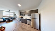 Located at 505 E St Louis St in Springfield, MO, this one-bedroom, one-bathroom unit offers a thoughtfully designed layout across a single floor. The open-concept kitchen and dining area is outfitted with dark espresso cabinetry reaching to the ceiling, light countertops, and a full suite of stainless steel appliances including a refrigerator, dishwasher, and range. Light wood-tone flooring runs throughout, contributing to a clean, contemporary aesthetic.

The spacious primary bedroom serves as the heart of the unit, accommodating a full sleeping area, a dedicated workspace, and a living area — all within a single well-proportioned room. A large floor-to-ceiling window floods the space with natural light and offers open views of the Springfield skyline, enhancing the sense of space. Pendant lighting adds a stylish, modern touch overhead.

The bathroom features a clean, minimalist design with wood-tone flooring, neutral walls, and a shower with a curtain enclosure. An in-unit laundry area adds everyday convenience. The overall ambiance is modern and functional, with a neutral palette and contemporary finishes that create a bright, livable environment well-suited for urban living in downtown Springfield.