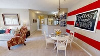 Located at 1201 Camellia Trace in Maryville, Tennessee, this single-floor residence offers a thoughtfully designed layout with a warm, welcoming ambiance throughout. The living room is bright and airy, featuring a ceiling fan, plush carpeting, and a fireplace flanked by an open shelving unit — an ideal spot for relaxing or entertaining. Adjacent to the living area, the kitchen is well-equipped with ample white cabinetry, a full suite of white appliances, laminate wood-style flooring, and a peninsula counter that provides both workspace and a natural transition into the dining area. The dining space is a standout, anchored by a bold red-and-white striped accent wall and an elegant chandelier that adds character and charm. The bedrooms are comfortably sized with soft carpeting, natural light from slatted windows, and generous closet space — including a walk-in closet in the primary bedroom. The bathroom features a tub-shower combination with clean, neutral finishes. A dedicated utility area houses the electrical panel and built-in shelving, adding practical functionality. The overall palette of warm beige tones and neutral walls creates a cohesive, inviting atmosphere throughout the home.