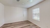 This single-floor residence presents a clean, modern aesthetic with thoughtful finishes throughout. The living area is bright and open, featuring light wood-look laminate flooring, crisp white walls, and a ceiling fan overhead. A large window fitted with blinds allows natural light to fill the space, creating a welcoming atmosphere. The entry door features a multi-point locking system, adding a layer of security.

The galley-style kitchen is a standout feature, offering generous storage through floor-to-ceiling grey cabinetry with brushed nickel hardware on both sides of the corridor. White quartz-style countertops provide ample workspace, while stainless steel appliances — including an electric range, over-the-range microwave, and refrigerator — complete the functional setup. A window at the end of the kitchen brings in additional natural light.

A secondary room with wood-look flooring, a ceiling fan, and dual windows offers a versatile space suitable for use as a bedroom or flex room. The bathroom is finished with large-format grey wall tiles surrounding a full soaking tub and shower combination, complemented by wood-look tile flooring and brushed nickel fixtures. Throughout, the neutral color palette and consistent flooring create a cohesive and inviting living environment.