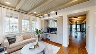 Located at 170 Graphics Drive in Madison, Alabama, this single-floor commercial space offers a well-appointed and cohesive interior blending modern farmhouse aesthetics with functional design. Rich hardwood flooring flows throughout, complemented by shiplap and wood-paneled ceilings with exposed beams that lend warmth and architectural character to each area.

The combined dining and living room serves as the heart of the space, featuring large multi-pane windows that flood the interior with natural light and offer outdoor views. The living area is anchored by a comfortable seating arrangement, while the dining area is defined by a statement woven pendant light above a marble-topped table with leather chairs. An integrated wet bar with dark countertops and soft gray cabinetry adds practicality and elegance.

The hallway is a standout architectural feature, lined with floor-to-ceiling glass-panel doors in a bold slate-gray finish, decorative star pendant fixtures, and a warm wood-planked ceiling — creating a striking corridor that connects the various rooms. Restroom facilities and a laundry area are conveniently accessible from this corridor. Throughout, the space maintains a bright, neutral palette accented by curated artwork, creating a refined and professional yet inviting ambiance.