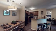 This single-floor residence offers a thoughtfully designed layout that balances comfort and functionality across its key living spaces. The kitchen is a standout feature, showcasing rich dark wood cabinetry, granite-style countertops, a mosaic tile backsplash, black appliances including a full-size refrigerator and range, and a breakfast bar with seating — all finished with durable wood-style flooring. Adjacent to the kitchen, the dining area provides space for a full dining table, creating a seamless flow into everyday living. The living room is warm and inviting, featuring wood-style flooring, a ceiling fan, built-in shelving, and a sliding glass door that opens to a private patio with outdoor views, filling the room with natural light. Two well-sized bedrooms feature plush carpet, ceiling fans, and generous windows. The primary bedroom connects to a private en suite bathroom with a walk-in shower and an elongated vanity corridor with built-in storage. A second full bathroom includes a tub-shower combination with tiled surround. The in-unit laundry room accommodates a full-size washer and dryer with additional shelf storage above. Throughout the residence, neutral warm tones and consistent finishes create a cohesive and comfortable atmosphere.