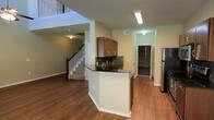 Located in Grand Prairie, Texas, this two-story home offers a thoughtfully designed layout that balances functionality and comfort. The main level showcases warm hardwood-style flooring that flows seamlessly throughout the open living areas, creating a cohesive and inviting atmosphere.

The kitchen serves as a central focal point, featuring rich wood cabinetry, dark stone countertops, and a decorative tile backsplash. A peninsula-style breakfast bar extends from the kitchen, providing additional prep space and casual seating. Stainless steel appliances complete the kitchen's modern appeal.

The open-concept design connects the kitchen to the main living area, which benefits from the vertical openness created by the two-story layout. A staircase with classic wood balusters leads to the upper level, adding architectural character to the space. The upper floor overlooks the main level, enhancing the sense of height and spaciousness.

A hallway off the kitchen leads to additional rooms, including what appears to be a pantry or storage area, adding practical utility to the home. Ceiling-mounted lighting and strategically placed vents ensure comfort and functionality throughout. The overall ambiance of the home is warm and welcoming, with a neutral color palette that provides a versatile backdrop for a variety of interior styles.