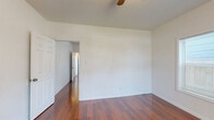 Located at 11 Norwood St in Houston, TX, this single-floor, 2-bedroom, 1-bathroom home offers a practical and efficient layout. Rich, warm-toned hardwood flooring runs continuously throughout the living areas and bedrooms, creating a cohesive and inviting feel. The entry area features a ceiling fan and a window that allows natural light to filter in. The primary bedroom is generously sized, offering ample room for furnishings, and is equipped with a ceiling fan for added comfort. The second bedroom also features hardwood floors and windows with blinds, including a window-unit air conditioner. The kitchen is thoughtfully appointed with white cabinetry, a double-basin sink with stone-look countertops, a black gas range with overhead ventilation, a full-size refrigerator, and a pantry closet. The kitchen also benefits from two windows that bring in natural light. The bathroom is clean and bright, finished with large-format tile flooring, a white vanity with sink, a soaking tub with tiled surround, and a window for ventilation. A hallway and closet complete the floor plan, providing functional storage and connectivity between rooms.