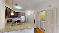 Located at 1109 Matteo Dr in Wilmington, NC, this single-floor residence offers a well-designed open-concept layout that seamlessly connects the kitchen and living areas. The kitchen is a standout feature, equipped with rich dark-stained cabinetry, granite countertops, and a full suite of stainless steel appliances including a refrigerator, electric range, and built-in microwave. A large kitchen island with an integrated sink and pendant lighting above serves as both a functional workspace and a casual dining or gathering spot. Warm hardwood flooring extends throughout the main living areas, creating a cohesive and inviting atmosphere. The spacious living room is bathed in natural light from sliding glass doors that lead to an outdoor area, and a ceiling fan adds comfort year-round. A dedicated in-unit laundry closet provides added convenience. The bathroom features tile flooring, a combination tub and shower, and a vanity with granite countertops consistent with the kitchen's finishes. A generously sized walk-in closet with built-in shelving and carpeted flooring completes the bedroom area. The layout is thoughtfully designed to maximize both functionality and comfort throughout.