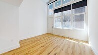 Located at 619 North Broad Street in Philadelphia's vibrant Northern Liberties neighborhood, this two-story residence offers a thoughtfully designed layout spread across two levels. The main floor features a bright, open-plan kitchen and living area bathed in natural light from large, floor-to-ceiling windows that frame street views of the surrounding cityscape. The kitchen is appointed with sleek white cabinetry, warm terracotta lower cabinets, stainless steel appliances, a tile backsplash, and a generous quartz island with an integrated sink and a brushed gold faucet, illuminated by modern pendant lighting. Exposed industrial-style ductwork adds a loft-like character to the living area, which features light-toned hardwood floors throughout. A private outdoor terrace off the main level provides an open-air retreat with brick detailing and tiled flooring. Upstairs, the bedroom offers a tranquil retreat with plush carpeting, clean white walls, a double closet, and an open railing overlooking the lower level. The full bathroom makes a bold design statement with striking gradient tile work in orange, gold, and cream tones surrounding a soaking tub and shower combination.