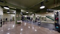 Located at 1200 W Winnemac Ave in Chicago's Ravenswood neighborhood, this two-floor fitness facility offers a well-equipped and thoughtfully designed workout environment. The space is distinguished by its industrial-chic aesthetic, featuring exposed ductwork and structural elements painted in deep green tones, polished concrete floors, and bold botanical-patterned wallcoverings that add a distinctive character throughout.

The main floor is expansive and open, housing a diverse array of strength and functional training equipment, including rowing machines, adjustable benches, cable machines, kettlebells, medicine balls, and a multi-use rack. Rubber flooring mats define dedicated workout zones, while large wall-mounted mirrors amplify the sense of space and support proper form during training. Pendant lighting casts focused illumination throughout the area.

A second floor, accessible via a green-railed staircase, extends the workout space further and features a dedicated cardio zone lined with treadmills and elliptical machines, each equipped with individual screens. This level maintains the same cohesive green-toned palette and polished flooring, with mirrored walls enhancing the open feel. Together, the two floors provide a comprehensive and visually cohesive fitness environment suited for a wide range of training needs.