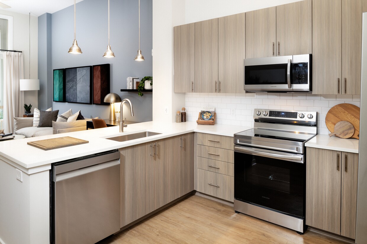 Cocina moderna con gabinetes de roble, placa para salpicaduras de azulejos blancos, encimeras de cuarzo blanco, electrodomésticos de acero inoxidable e iluminación colgante. - Avalon Durham