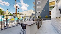 Located at 1022 S Oxford Ave in the Koreatown neighborhood of Los Angeles, this outdoor amenity space is a thoughtfully designed courtyard that serves as a central gathering hub for residents. The space is anchored by a resort-style swimming pool, surrounded by lounge seating and colorful mural accents that add a vibrant, artistic character to the environment.

Adjacent to the pool area, a dedicated outdoor kitchen and grilling station features a built-in bar counter with barstool seating and a full-sized gas grill, making it ideal for casual entertaining and al fresco dining. A separate outdoor dining area with a slatted table and chairs provides additional space for group meals in an open-air setting.

The courtyard is framed by the multi-story residential building on multiple sides, creating an enclosed and private atmosphere while still allowing for ample natural light and open sky views. Raised concrete planters filled with drought-tolerant plants, including striking yucca specimens, line the perimeter, contributing a clean and modern aesthetic.

Decorative geometric patterned tilework accents structural columns, adding a distinctive design detail to the hardscape. Wide concrete pathways throughout the courtyard ensure easy circulation between amenity zones. Gated entry points with secure fencing maintain safety and privacy. The overall ambiance is contemporary and community-oriented, offering residents a well-appointed outdoor retreat in the heart of Los Angeles.