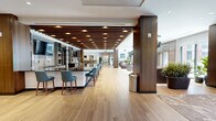 Located at 777 Summer St in Stamford, Connecticut, this thoughtfully designed amenity floor spans a generous footprint and offers a diverse collection of entertainment and social spaces. The welcoming main lounge sets the tone with wide-plank light wood flooring, warm walnut columns with wood-beam ceiling accents, pendant cluster lighting, and floor-to-ceiling windows that flood the space with natural light and provide views of an outdoor terrace. Curved, contemporary seating arrangements anchored by a textured area rug create an inviting atmosphere for gathering.

The game room features a full-size billiards table alongside a shuffleboard table, set against light hardwood floors and illuminated by recessed lighting and dramatic accent spotlights. A dedicated poker room makes a bold statement with richly patterned botanical wallcovering, a custom round poker table, and leather seating.

A sophisticated screening room is finished in deep burgundy walls with plush grey lounge chairs arranged for an immersive viewing experience. Adjacent, a golf simulator room — outfitted with a putting green, Full Swing simulator, and built-in walnut cabinetry — provides a premium recreational retreat.

The kitchen is finished with rich walnut cabinetry, black marble countertops and backsplash, and stainless steel appliances, offering full catering support for events throughout the floor.