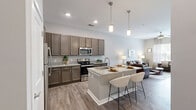 Located at 301 Continental Parkway in Newport News, Virginia, this one-bedroom, one-bathroom residence offers a thoughtfully designed single-floor layout that maximizes comfort and functionality. The open-concept living area is bathed in natural light from large windows dressed with elegant sheer curtains and blinds, creating a bright and welcoming atmosphere. Wood-look plank flooring flows throughout the main living spaces, lending a warm, cohesive aesthetic. A ceiling fan adds practicality to the airy living room.

The kitchen is a standout feature, showcasing rich taupe cabinetry, granite countertops, stainless steel appliances, and a central island with a built-in sink and pendant lighting overhead — ideal for both everyday cooking and casual dining.

The bedroom offers a cozy retreat with soft carpeting, a large window overlooking the outdoors, and neutral gray walls that create a calm, restful environment.

The bathroom is finished with wood-look tile flooring, a dark-toned vanity with granite counters, and a full tub-shower combination with a stylish patterned curtain. Clean, neutral tones throughout the entire residence contribute to a cohesive and modern living experience.