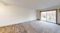 Located in Little Canada, MN, this two-bedroom, one-bathroom unit offers a well-organized single-floor layout designed for comfortable everyday living. The galley-style kitchen is thoughtfully arranged with warm wood cabinetry lining both walls, white appliances including a range and refrigerator, a built-in dishwasher, a double sink with ample counter space, and light wood-look flooring underfoot. A ceiling fan and overhead fluorescent lighting keep the space bright and comfortable. The kitchen flows toward a combined living area, where light-toned carpet transitions from the hard-surface entry. A sliding glass door fills the living room with natural light and provides direct access to a private balcony with outdoor views. Both bedrooms are carpeted and feature baseboard heating, neutral walls, and access to closet storage — one of which is a spacious walk-in closet with built-in shelving and hanging rods. The full bathroom includes a tiled tub-and-shower combination, mosaic tile flooring, a vanity with wood cabinetry, and clean, simple finishes throughout. The unit's understated, functional design offers a solid foundation for personalization in a quiet suburban setting.