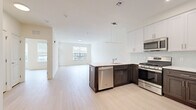 This thoughtfully designed two-bedroom, one-bathroom unit offers a clean, modern aesthetic across a single floor. The open-concept living and kitchen area serves as the heart of the unit, where light hardwood-style flooring and crisp white walls create a bright, airy atmosphere. Large windows in the living area allow abundant natural light to fill the space while providing views of the surrounding neighborhood.

The kitchen is a standout feature, showcasing a two-tone design with dark espresso lower cabinets paired with white upper shaker-style cabinetry. A peninsula with a light quartz countertop provides additional workspace and casual seating potential. Stainless steel appliances, including a gas range, microwave, dishwasher, and refrigerator, complete the well-appointed kitchen, which also features a light tile backsplash.

Both bedrooms are finished with the same light flooring and neutral walls, offering a calm, versatile canvas. The primary bedroom is a comfortable size, while the second bedroom provides flexible use. The bathroom features wood-look tile flooring, large-format stone-style wall tiles surrounding the soaking tub and shower combination, and a white vanity with a quartz countertop, delivering a polished, spa-like finish.