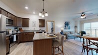 Parkview Grand's 2-bedroom, 2-bathroom floor plan delivers a well-appointed, single-floor layout designed for comfortable everyday living. The open-concept kitchen is a standout feature, showcasing rich dark wood cabinetry, granite countertops, and a full suite of stainless steel appliances including a range, microwave, and refrigerator. A center island with bar seating flows seamlessly into the living area, making it ideal for both casual dining and entertaining. The living room is generously proportioned, featuring light wood-style flooring, a ceiling fan, and a sliding glass door that opens to a private balcony with expansive outdoor views. Both bedrooms are well-sized and carpeted, offering a quiet retreat. The primary bedroom includes direct access to an en-suite bathroom, while the second bathroom features a full tub-shower combination. A dedicated in-unit laundry room with a full-size washer and dryer adds everyday convenience. Recessed lighting and neutral-toned walls throughout create a bright, welcoming atmosphere that complements the home's modern yet warm aesthetic.