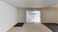This single-story residence offers a clean, functional layout designed for comfortable everyday living. The living area serves as the heart of the home, featuring neutral carpet flooring that transitions to wood-look flooring near the entryway. A large sliding glass door fitted with vertical blinds fills the space with natural light and provides direct access to an outdoor patio, offering views of the surrounding landscape. A dedicated front entry door sits adjacent to the sliding door, creating a welcoming entryway.

The kitchen is equipped with white cabinetry, a double-basin stainless steel sink, light-toned countertops, and wood-look flooring. Upper and lower cabinet storage provide ample organization space throughout.

A carpeted hallway connects the living areas to the private quarters, leading to multiple bedrooms. Each bedroom features neutral carpet, white walls, a textured ceiling, and its own closet with built-in shelving. Windows dressed with vertical blinds allow natural light into these rooms.

The bathrooms include a vanity with white cabinetry, a lighted mirror, and light countertops, while a separate full bathroom features a tub-shower combination and wood-look flooring. Throughout, the space maintains a consistently neutral, light-toned palette with textured ceilings, creating a clean and practical living environment.