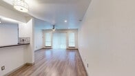 This single-floor unit offers a clean, contemporary layout designed for comfortable everyday living. The living area is an open, airy space anchored by warm wood-look flooring that extends throughout the unit, recessed lighting, and a ceiling fan that enhances air circulation. A sliding glass door flanked by two windows allows generous natural light to fill the room while providing outdoor access. Vertical blinds and window blinds offer privacy and light control.

The kitchen is thoughtfully designed with white cabinetry, dark granite-style countertops, a mosaic tile backsplash, and a suite of stainless steel appliances including a refrigerator, range, and microwave. A breakfast bar-style pass-through connects the kitchen to the main living space, and a track lighting fixture above ensures the area is well-lit.

The bedroom is a generously sized, quiet retreat with its own ceiling fan, recessed lighting, and a large window that brings in natural light. A dedicated laundry area features a stacked washer unit conveniently positioned adjacent to the bathroom, which includes a vanity with dark countertops and white cabinetry. The unit's neutral color palette and consistent flooring create a cohesive, move-in-ready atmosphere throughout.