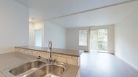 This clean and contemporary single-floor unit is designed with a functional, open-concept layout that seamlessly connects the kitchen and living areas. The kitchen is well-equipped with stainless steel appliances, including a refrigerator, electric range, over-the-range microwave, and dishwasher. Two-tone cabinetry pairs white upper cabinets with warm wood-toned lower cabinets, complemented by subway tile backsplash and quartz-style countertops. A double stainless steel sink and a tile-accented peninsula add practical workspace to the kitchen.

The open living area flows naturally from the kitchen and is finished with light wood-tone laminate flooring throughout. Large sliding glass doors lead to a private balcony that overlooks lush greenery, filling the space with natural light and a refreshing outdoor connection. The living area is bright and clean with neutral white walls and recessed lighting.

The bedroom is a quiet, carpeted retreat with a window that brings in soft natural light and a baseboard heater for year-round comfort. The bathroom features a tub-shower combination with tile surround, wood-tone flooring, and clean white finishes, offering a simple and functional design. Overall, the unit presents a modern, move-in-ready aesthetic with consistent finishes throughout.