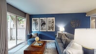 This thoughtfully designed single-floor residence offers a cohesive blend of contemporary style and functional living. The living room serves as the centerpiece, featuring a striking deep blue accent wall adorned with a triptych of abstract artwork, a brick fireplace, and a sliding glass door that opens to a private outdoor patio, filling the space with natural light. The galley-style kitchen is well-appointed with rich dark cabinetry, granite-style countertops, stainless steel appliances, wood-look flooring, and a dedicated pantry for ample storage. Adjacent to the kitchen, the dining area offers a welcoming space for meals, highlighted by large windows with floor-length drapes and complementary blue-gray accent walls. The primary bedroom features a ceiling fan, plush carpeting, a bold blue accent wall, and direct access to a well-finished bathroom complete with dark wood vanity cabinetry, granite countertops, and a tub-shower combination. A secondary bedroom mirrors the comfortable carpeted design with its own ceiling fan and generous natural light. Completing the layout is a convenient in-unit laundry closet with side-by-side washer and dryer, framed by louvered doors and built-in shelving for added organization.