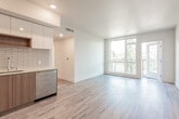 This contemporary single-floor residence showcases a clean, modern design with light-toned hardwood flooring that runs seamlessly throughout the entire space. The open-concept living and kitchen area forms the heart of the unit, offering a bright and airy atmosphere enhanced by large windows and a glass door that opens to a private balcony with lush tree canopy views beyond.

The kitchen is thoughtfully designed with a two-tone cabinetry scheme — warm wood lower cabinets paired with sleek, light-colored upper cabinets — complemented by a white subway tile backsplash, light quartz countertops, a stainless steel undermount sink, and a full suite of stainless steel appliances including a gas range, over-the-range microwave, and French door refrigerator.

Multiple bedrooms offer generous natural light through floor-to-ceiling and oversized windows, each framing tranquil views of surrounding trees and the neighborhood roofscape below. Recessed lighting adds a clean, finished look to the ceilings.

Two bathrooms serve the space: one full bath featuring a soaking tub with a curved shower rod and full subway tile surround with built-in wall niches, and a second bath with a floating wood vanity, large mirror, and a bright window. Both bathrooms continue the hardwood flooring and maintain the residence's cohesive modern aesthetic.