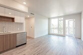 This contemporary single-floor residence showcases a clean, modern design with light-toned hardwood flooring that runs seamlessly throughout the entire space. The open-concept living and kitchen area forms the heart of the unit, offering a bright and airy atmosphere enhanced by large windows and a glass door that opens to a private balcony with lush tree canopy views beyond.

The kitchen is thoughtfully designed with a two-tone cabinetry scheme — warm wood lower cabinets paired with sleek, light-colored upper cabinets — complemented by a white subway tile backsplash, light quartz countertops, a stainless steel undermount sink, and a full suite of stainless steel appliances including a gas range, over-the-range microwave, and French door refrigerator.

Multiple bedrooms offer generous natural light through floor-to-ceiling and oversized windows, each framing tranquil views of surrounding trees and the neighborhood roofscape below. Recessed lighting adds a clean, finished look to the ceilings.

Two bathrooms serve the space: one full bath featuring a soaking tub with a curved shower rod and full subway tile surround with built-in wall niches, and a second bath with a floating wood vanity, large mirror, and a bright window. Both bathrooms continue the hardwood flooring and maintain the residence's cohesive modern aesthetic.